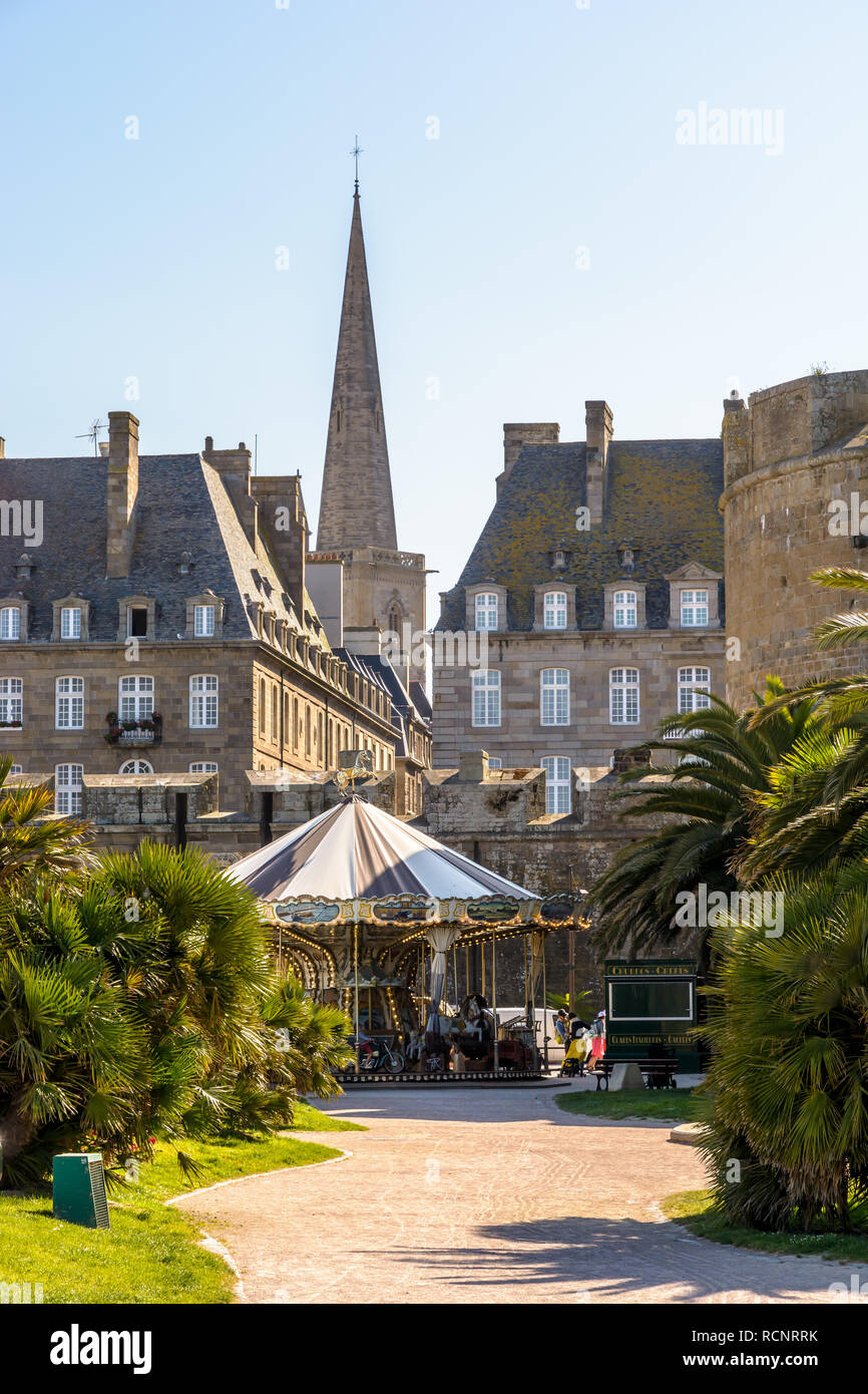 Un carrousel de style vintage à Saint-Malo en Bretagne, France, avec le clocher de la cathédrale Saint-Vincent coller dehors au-dessus des bâtiments au coucher du soleil. Banque D'Images