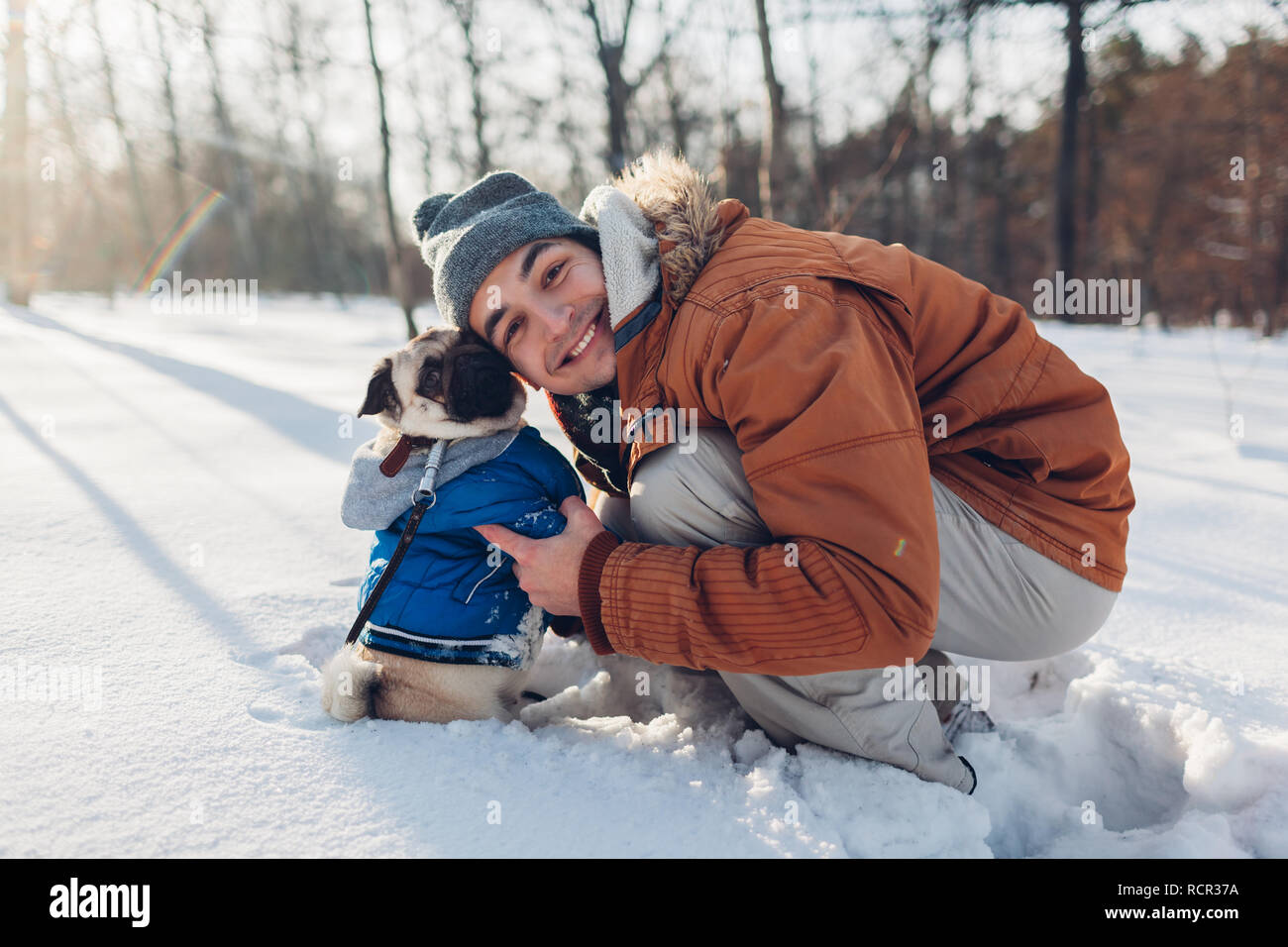 Le PUG dog walking sur la neige avec son maître. Chiot portant manteau d'hiver. Man hugging son animal en forêt d'hiver. Vêtements pour animaux Banque D'Images