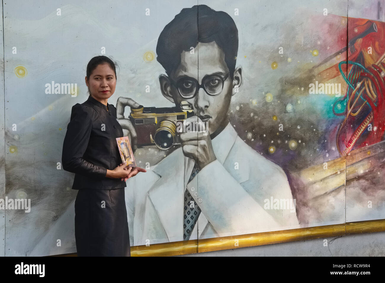 Après la mort du Roi Bhumipol, un deuil pose devant une peinture murale représentant le jeune roi que avid photographe avec son Leica ; à Bangkok Banque D'Images