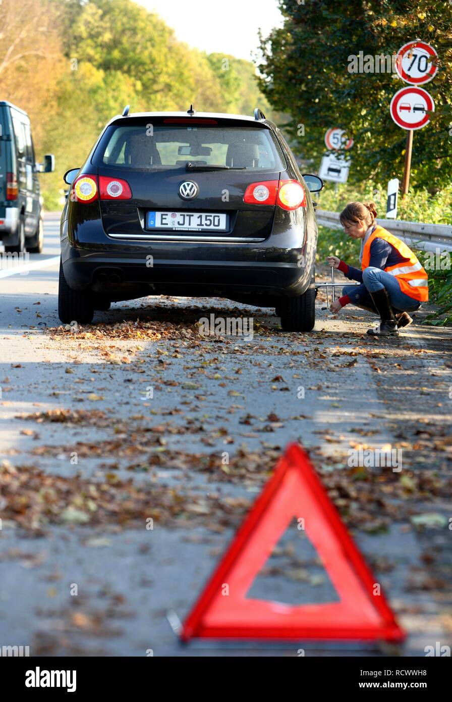 Triangle d'avertissement, panne de voiture, la conductrice s'est arrêtée sur la bande d'arrêt d'une route de campagne, portant un gilet réfléchissant Banque D'Images Triangle d'avertissement, panne de voiture, la conductrice s'est arrêtée sur la bande d'arrêt d'une route de campagne, portant un gilet réfléchissant Banque D'Images
