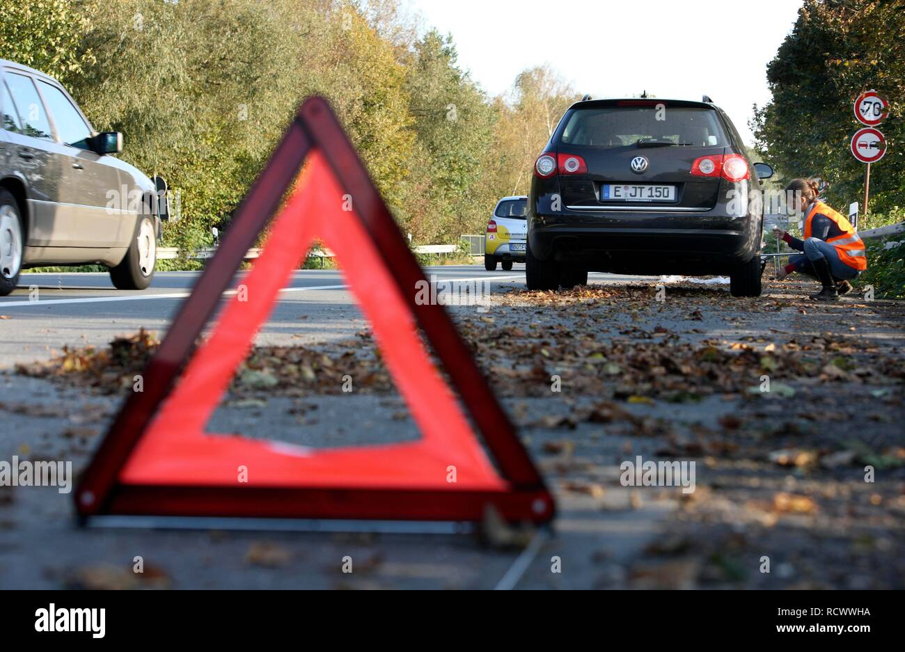 Triangle d'avertissement, panne de voiture, la conductrice s'est arrêtée sur la bande d'arrêt d'une route de campagne, portant un gilet réfléchissant Banque D'Images Triangle d'avertissement, panne de voiture, la conductrice s'est arrêtée sur la bande d'arrêt d'une route de campagne, portant un gilet réfléchissant Banque D'Images