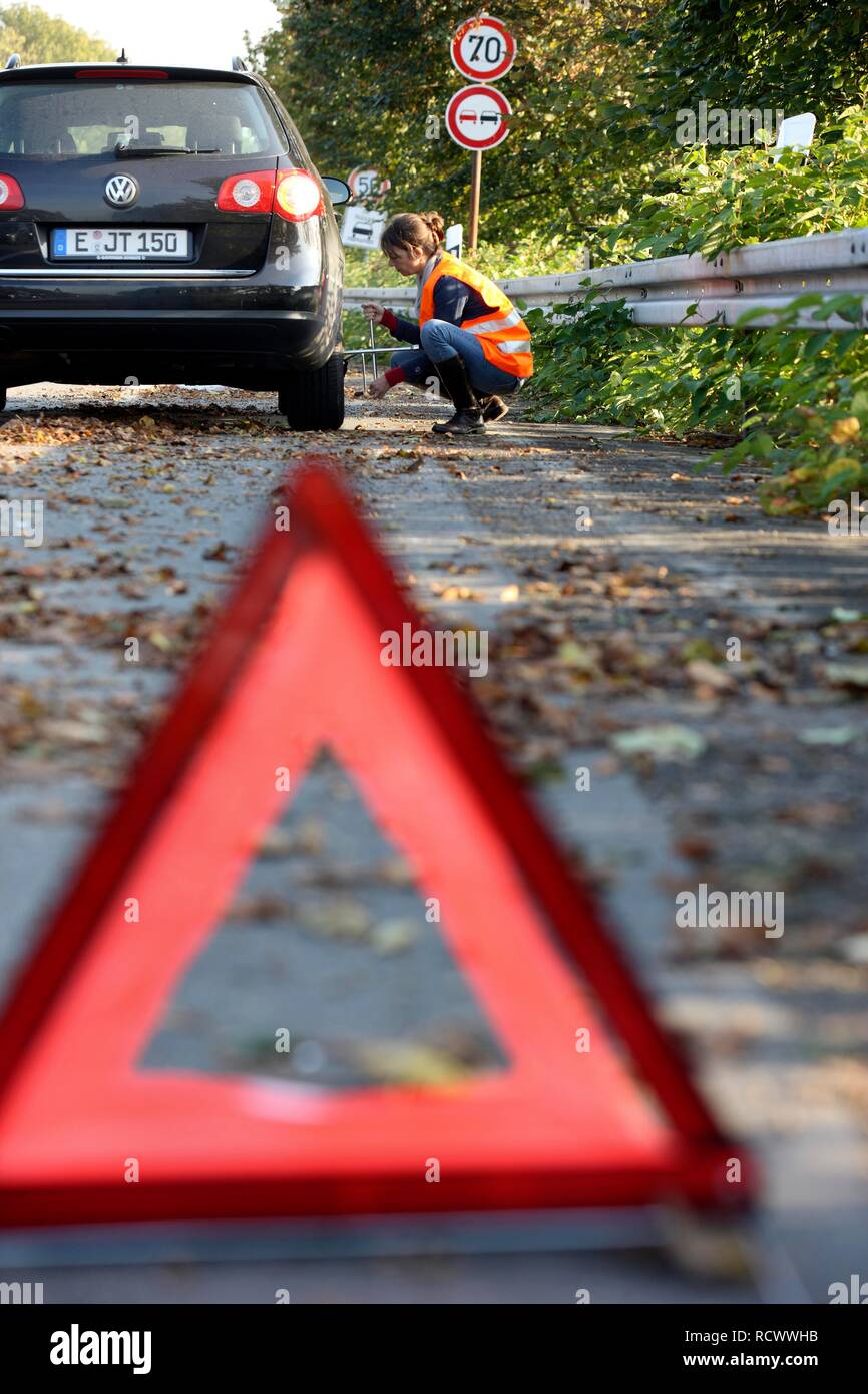 Triangle d'avertissement, panne de voiture, la conductrice s'est arrêtée sur la bande d'arrêt d'une route de campagne, portant un gilet réfléchissant Banque D'Images Triangle d'avertissement, panne de voiture, la conductrice s'est arrêtée sur la bande d'arrêt d'une route de campagne, portant un gilet réfléchissant Banque D'Images