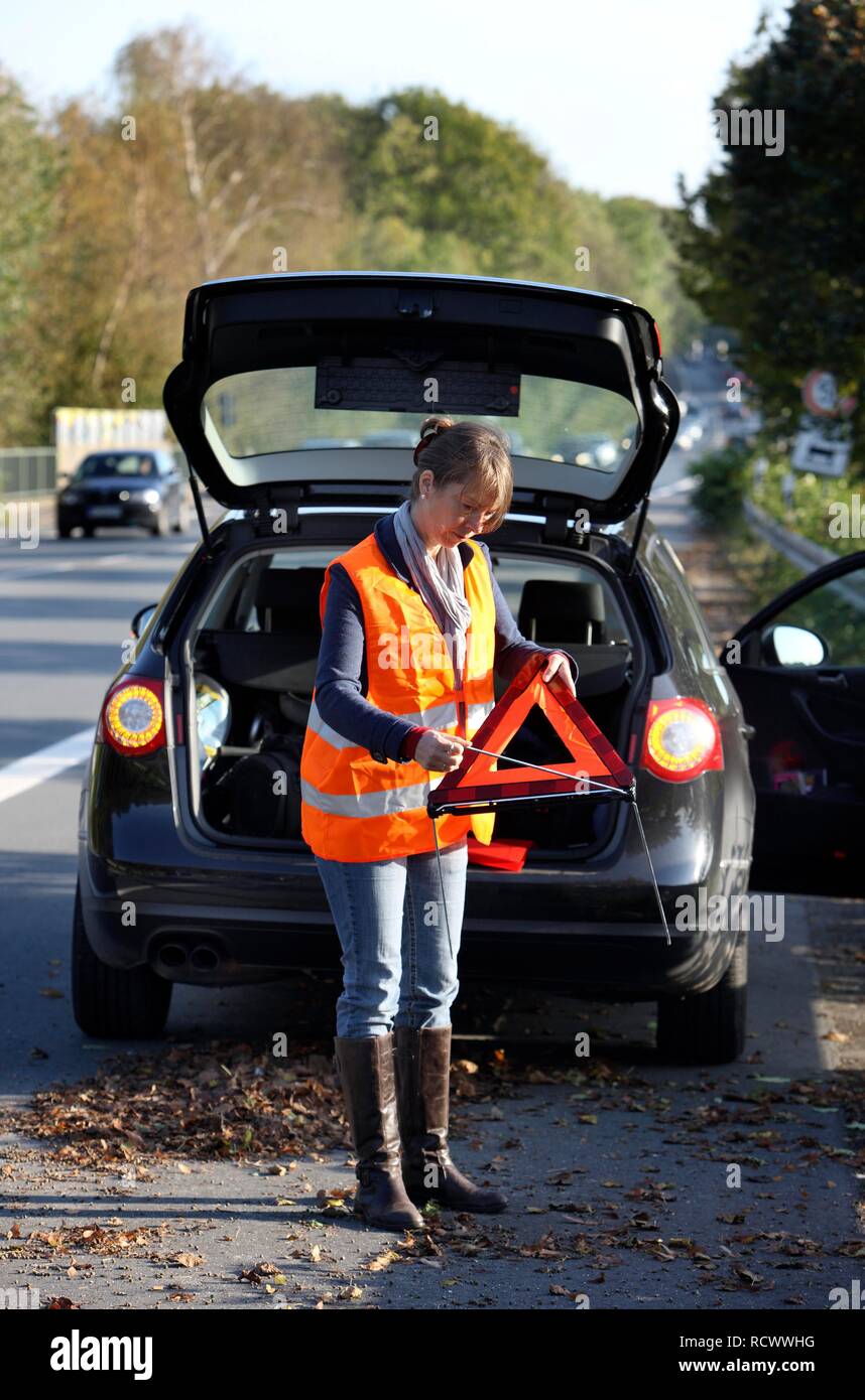 Panne de voiture, femme pilote sur la bande d'arrêt d'une route de campagne, portant un gilet réfléchissant, la mise en place d'un triangle d'avertissement Banque D'Images Panne de voiture, femme pilote sur la bande d'arrêt d'une route de campagne, portant un gilet réfléchissant, la mise en place d'un triangle d'avertissement Banque D'Images
