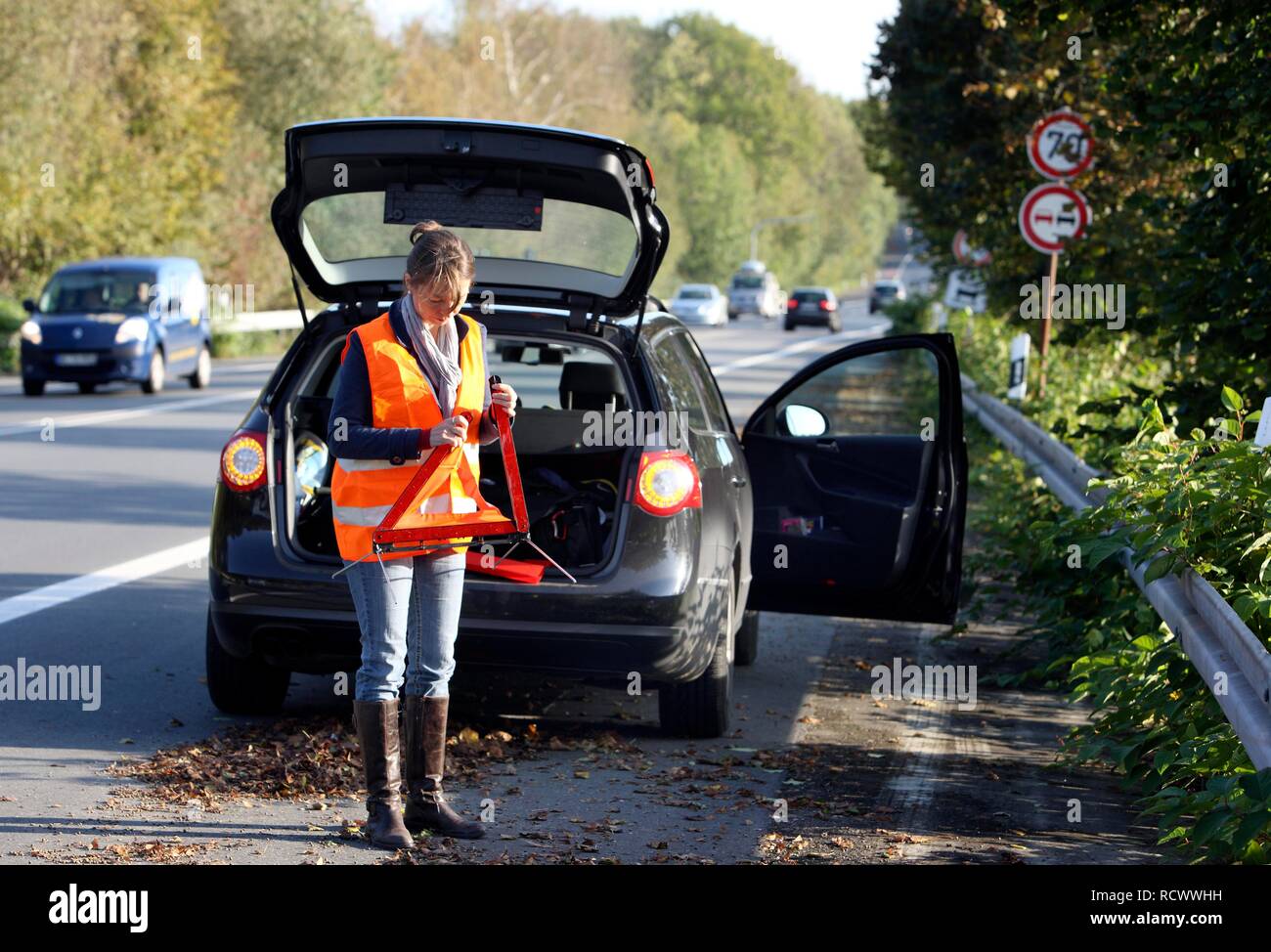 Panne de voiture, femme pilote sur la bande d'arrêt d'une route de campagne, portant un gilet réfléchissant, la mise en place d'un triangle d'avertissement Banque D'Images Panne de voiture, femme pilote sur la bande d'arrêt d'une route de campagne, portant un gilet réfléchissant, la mise en place d'un triangle d'avertissement Banque D'Images