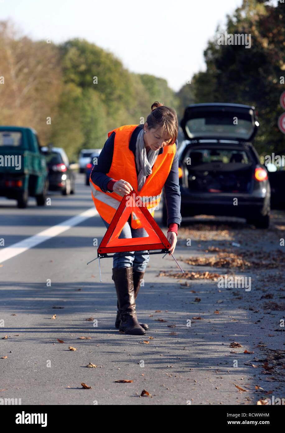 Panne de voiture, la conductrice s'est arrêtée sur la bande d'arrêt d'une route de campagne, portant un gilet réfléchissant Banque D'Images Panne de voiture, la conductrice s'est arrêtée sur la bande d'arrêt d'une route de campagne, portant un gilet réfléchissant Banque D'Images