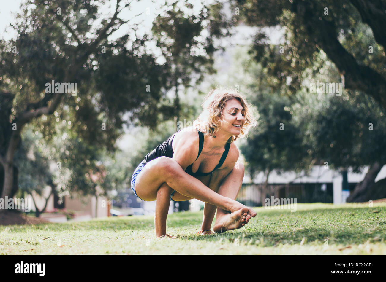 Smiling caucasian woman performing yoga tout en exerçant une pression sur l'épaule poser sur pelouse verte. Banque D'Images