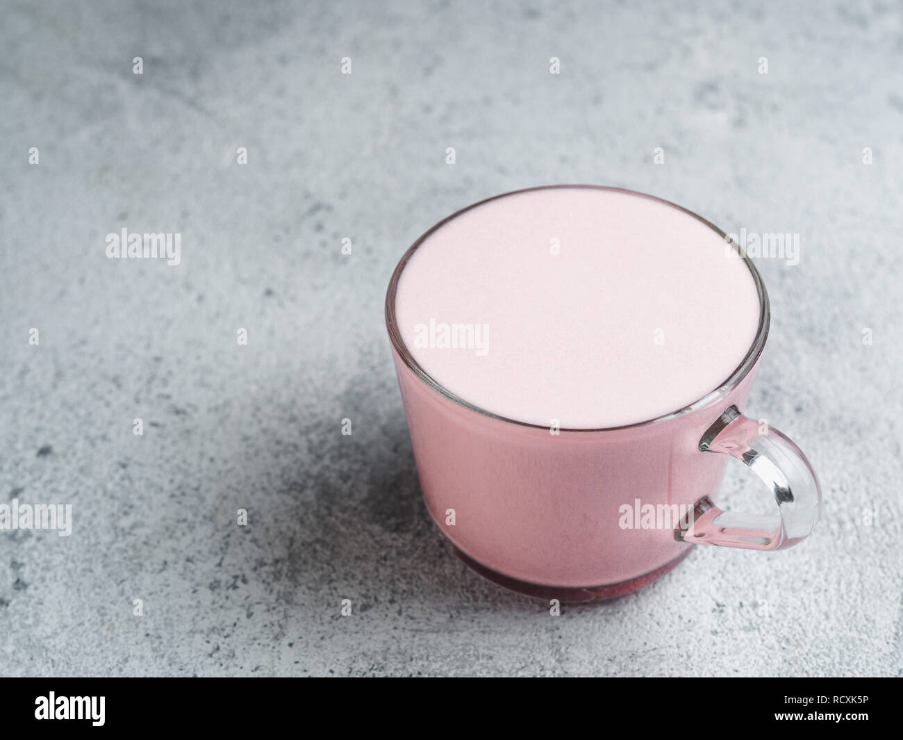 Boisson à la mode : pink latte. Framboises ou betterave cappuccino ou latte dans verre tasse sur fond de ciment gris. L'espace de copie pour le texte. Banque D'Images