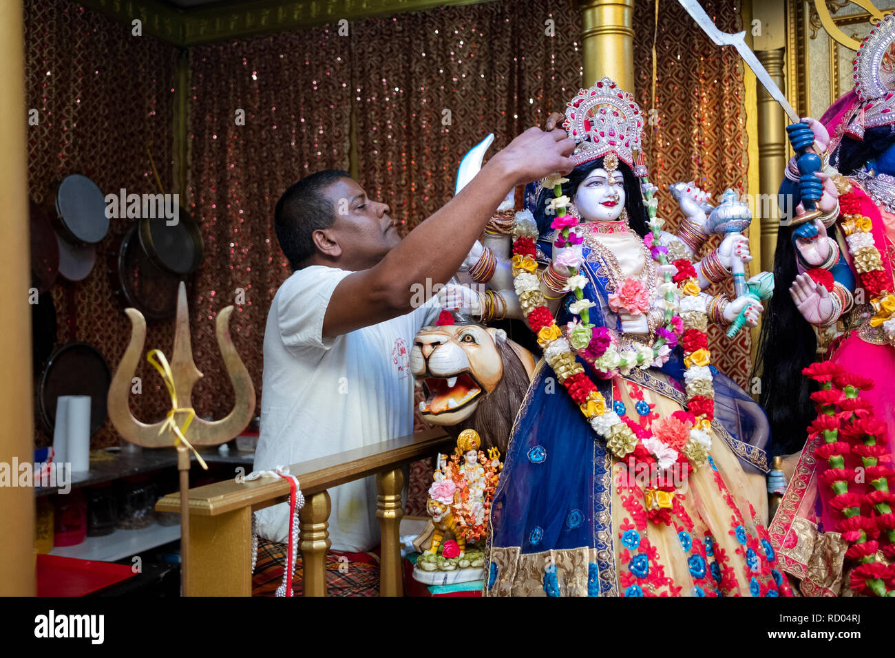 Un hindou pieux adorateur décorer une statue de la Déesse Durga avec fleurs. En Ozone Park, Queens, New York. Banque D'Images