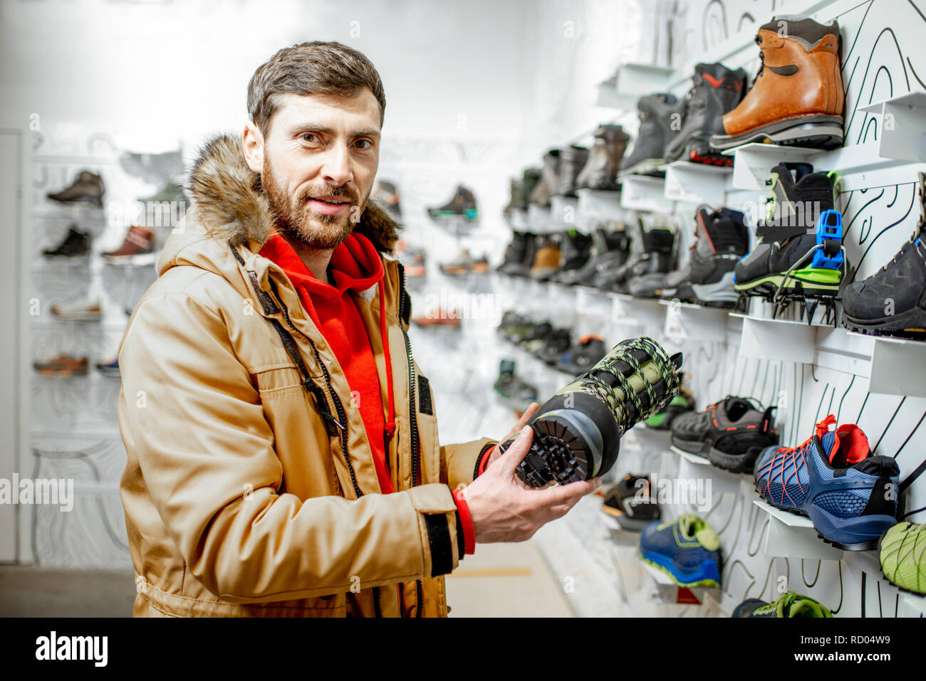 Portrait d'un homme en manteau d'hiver le choix de chaussures de trail pour la randonnée dans le magasin de sport Banque D'Images