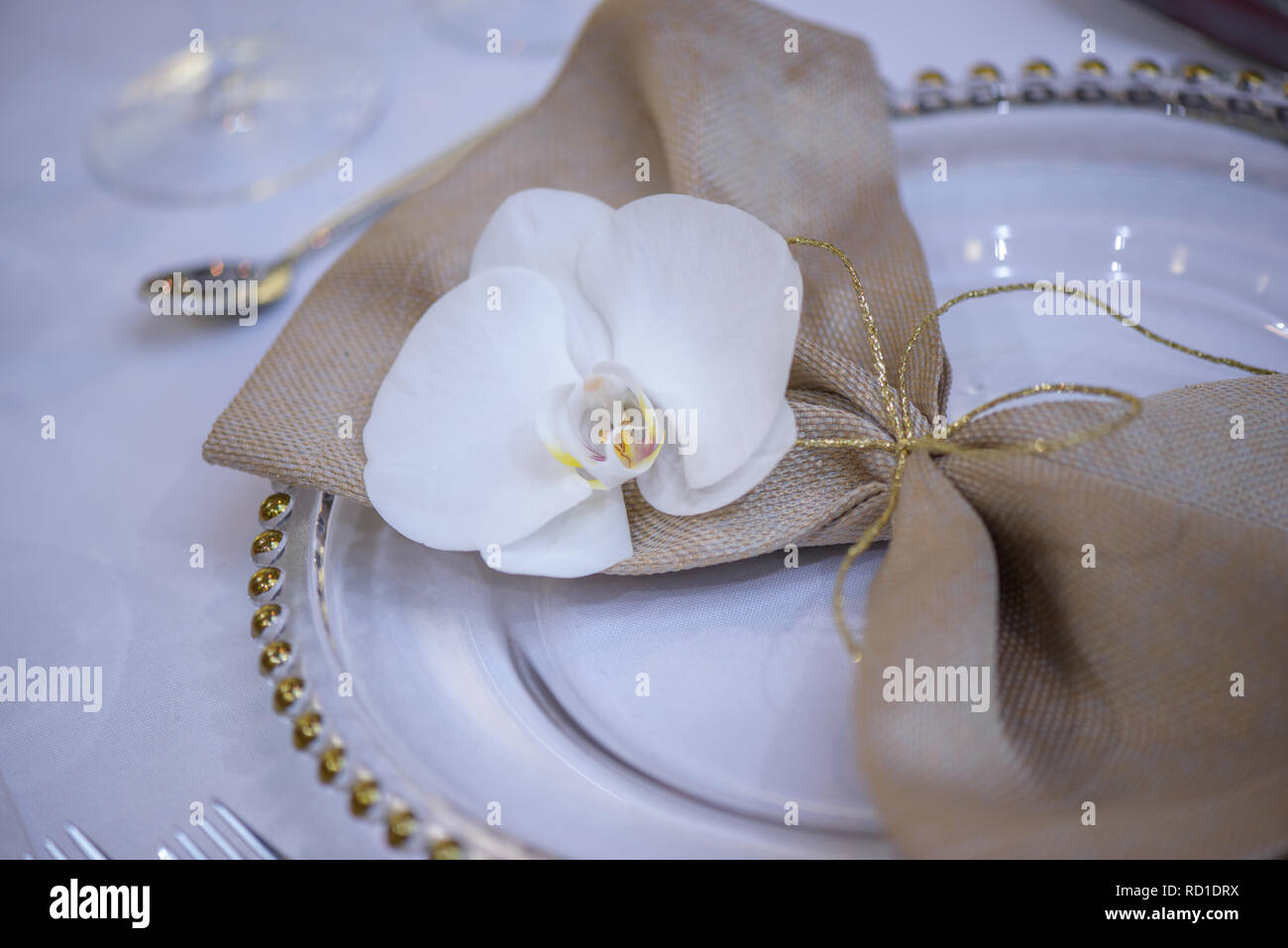 Belle table à manger avec plaques transparentes, lin naturel avec serviette orchidée et décorations d'or prêt pour les invités à un mariage Banque D'Images