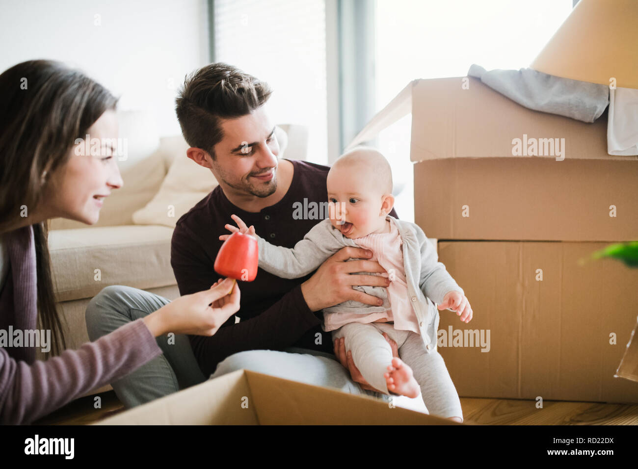 Jeune couple avec un bébé et des boîtes en carton déménagement dans une nouvelle maison. Banque D'Images