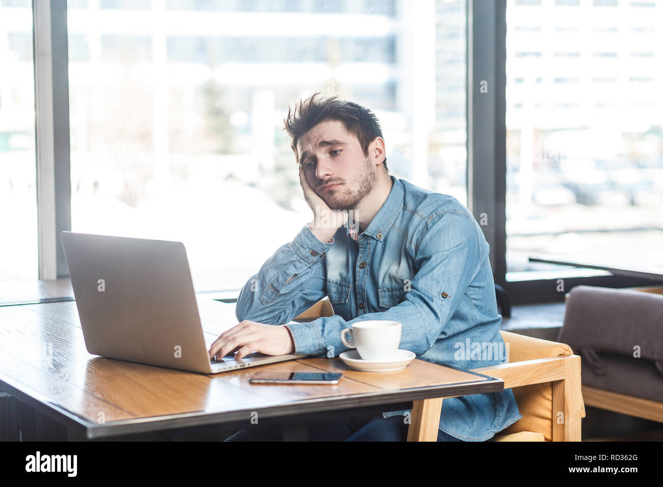 Je ne sais pas ! Portrait de tristesse fatiguée jeune barbu freelancer dans blue jeans chemise sont assise seule dans un café et la recherche d'un travail sur l'ordinateur portable sont dans Banque D'Images