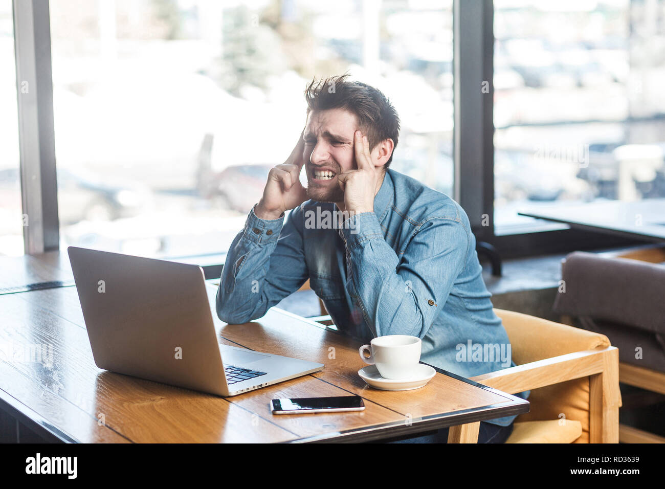 Être en attente d'une idée ! Vue de côté portrait de jeunes barbus réfléchie freelancer dans blue jeans chemise sont assis dans un café et travailler sur ordinateur portable, fermé ey Banque D'Images