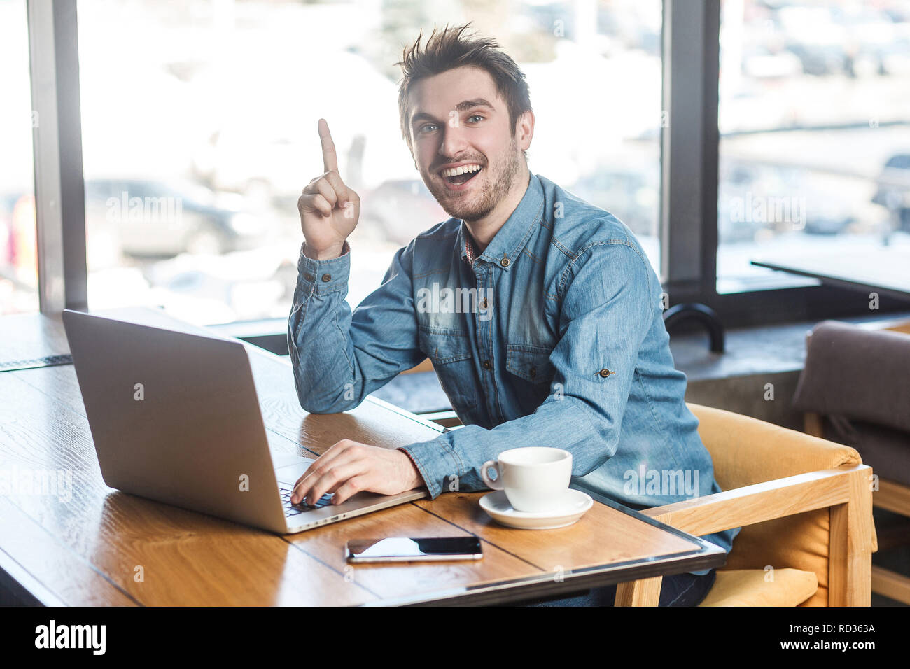 Avoir idée ! Portrait de jeunes barbus positive creative freelancer dans blue jeans chemise sont assis dans un café et travailler sur ordinateur portable avec sourire et dentelée Banque D'Images