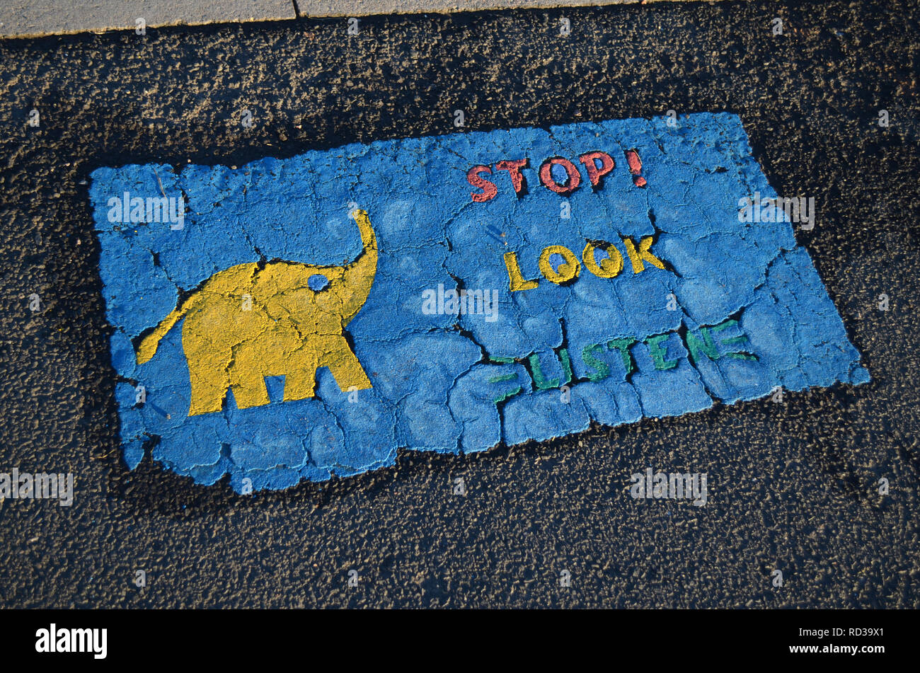 Weathered signe sur le trottoir pour les enfants à lire, arrêter, regarder, écouter, avec un éléphant jaune. Banque D'Images