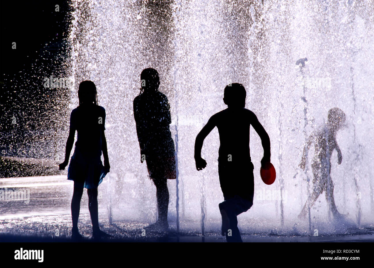 Silhouette de quatre enfants jouant dans une fontaine d'eau sur une journée chaude, United States Banque D'Images