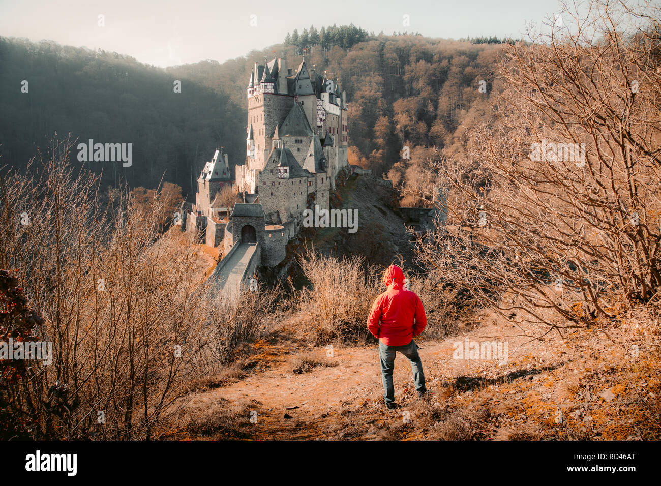 Vue panoramique de jeune en veste rouge en face du célèbre château d'Eltz allumé dans la belle lumière du matin au lever du soleil à l'automne, Rheinla Banque D'Images