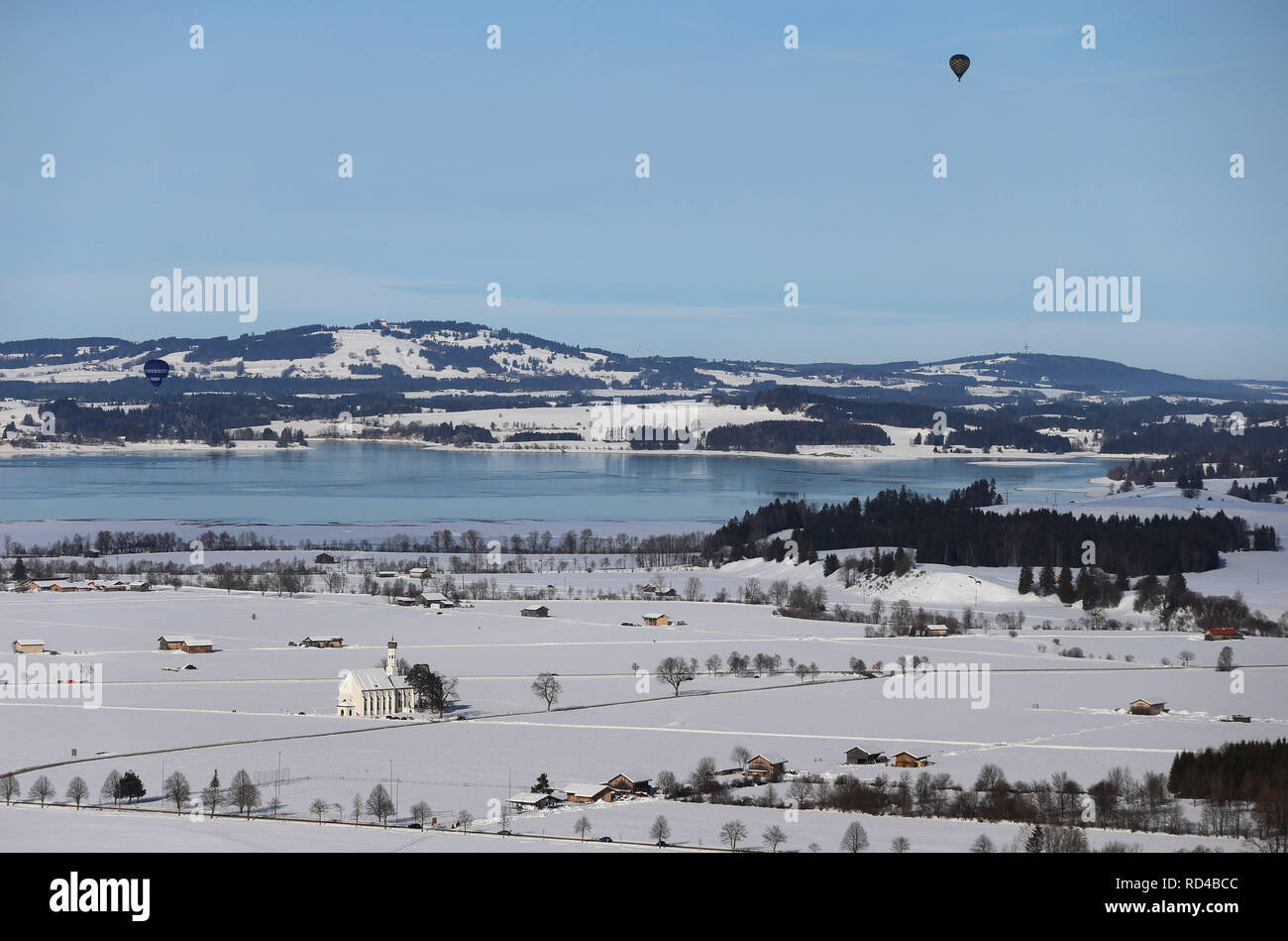 16 janvier 2019, la Bavière, Schwangau : ballons à air chaud sont battant sur le lac de Forggen et le sanctuaire de St Coloman, qui se dresse dans un paysage couvert de neige. Photo : Karl-Josef Opim/dpa Banque D'Images