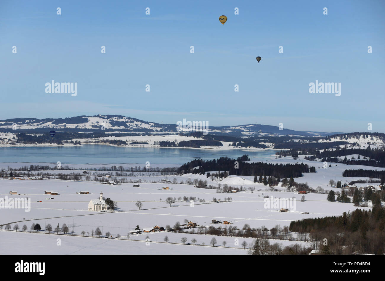 16 janvier 2019, la Bavière, Schwangau : ballons à air chaud sont battant sur le lac de Forggen et le sanctuaire de St Coloman, qui se dresse dans un paysage couvert de neige. Photo : Karl-Josef Opim/dpa Banque D'Images