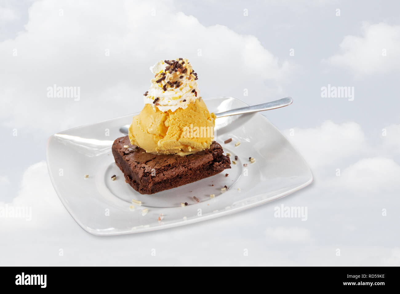 Dessert céleste avec la crème glacée, crème fouettée, sprinkles, brownie au chocolat blanc et sur la plaque de fond de nuage pâle, Banque D'Images