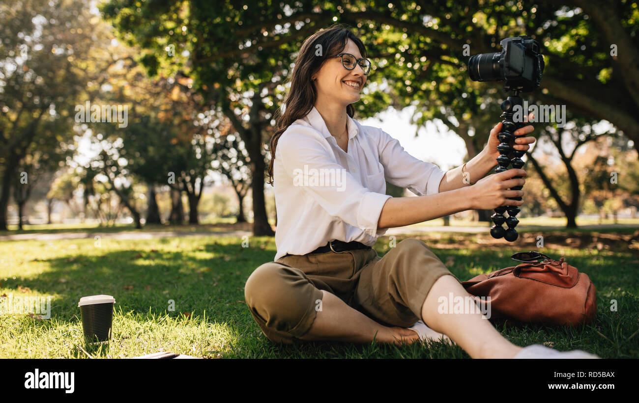 Femme blogger faire une vidéo à l'aide d'un appareil photo numérique monté sur trépied flexible. Jeune femme vlogging à partir d'un parc. Banque D'Images