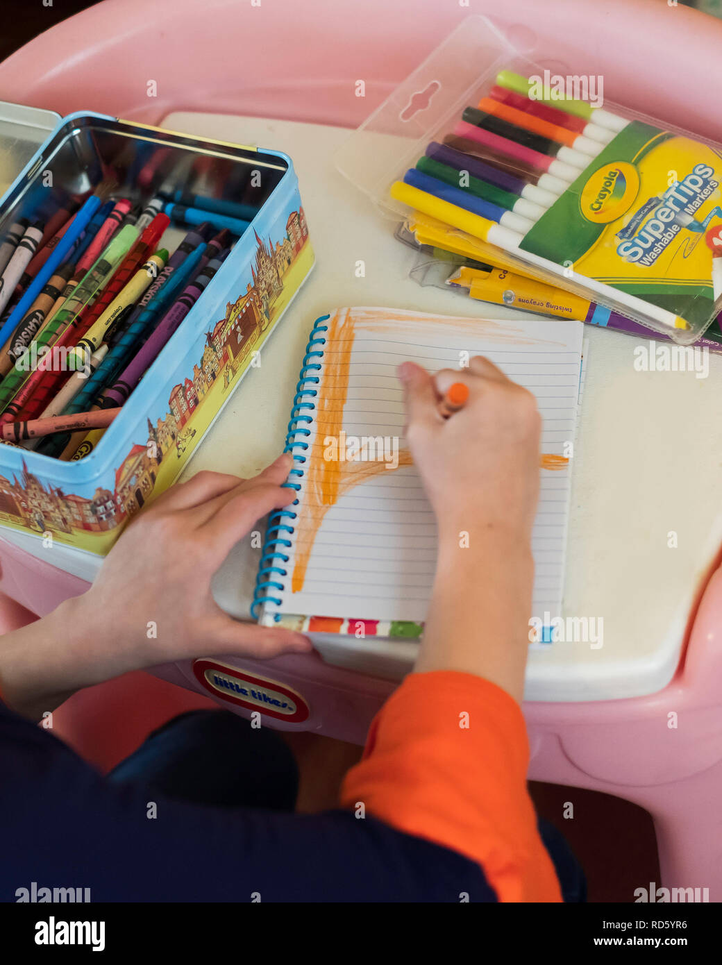 A 5 ans girl's hands coloring dans un ordinateur portable de marque Crayola crayons. Marque Crayola Marqueurs lavables dans un paquet. Banque D'Images