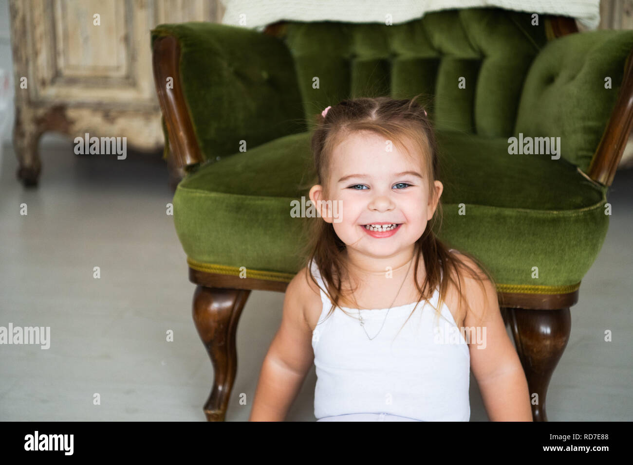 Portrait d'un rire heureux enfant fille assise sur le plancher près de la chaise ancienne Banque D'Images