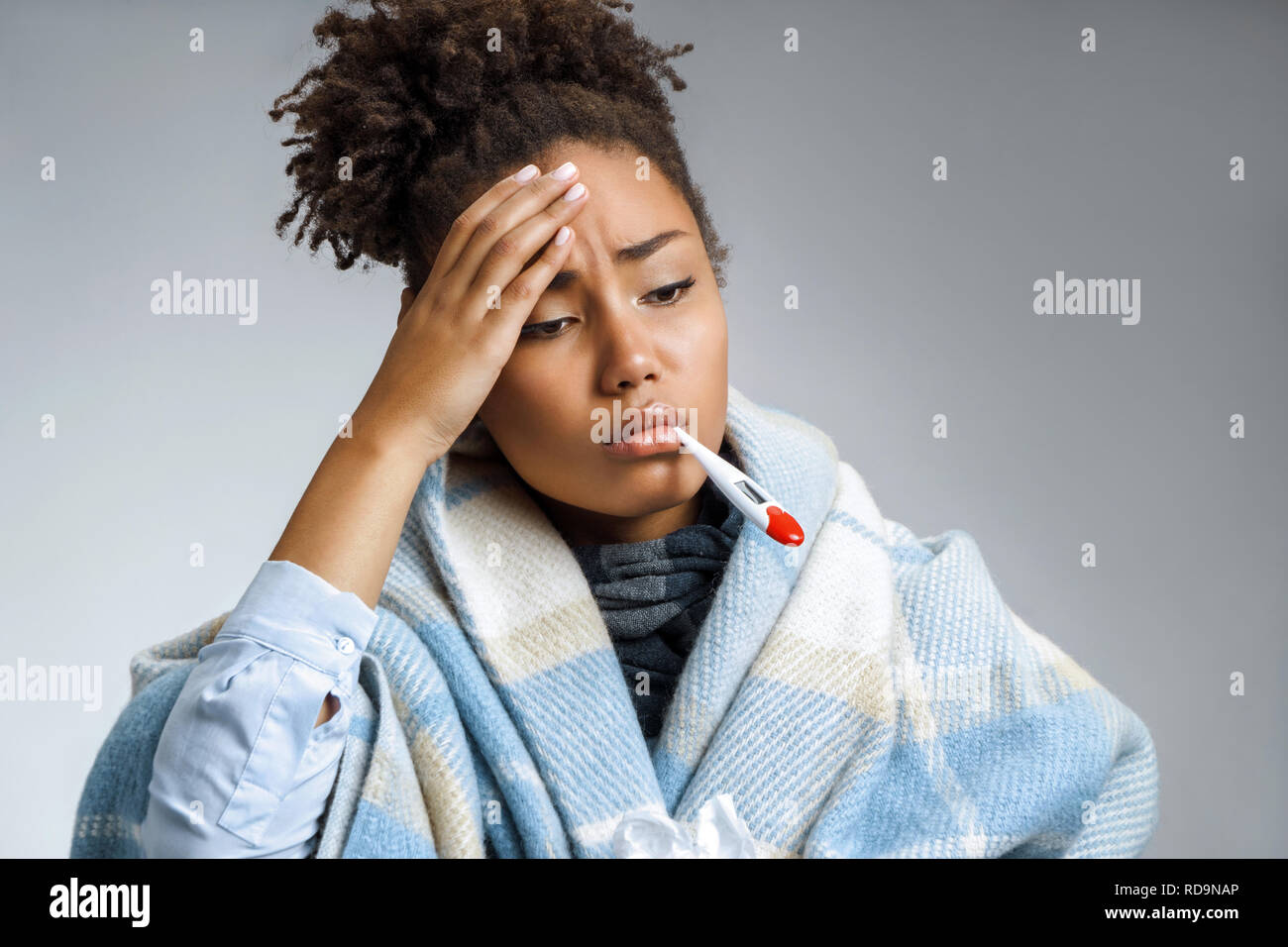 Femme malade avec le thermomètre dans la bouche, enveloppés dans de plaid.  Photo de african american woman wrapped in payé sur fond gris. Concept de  soins de santé Photo Stock - Alamy