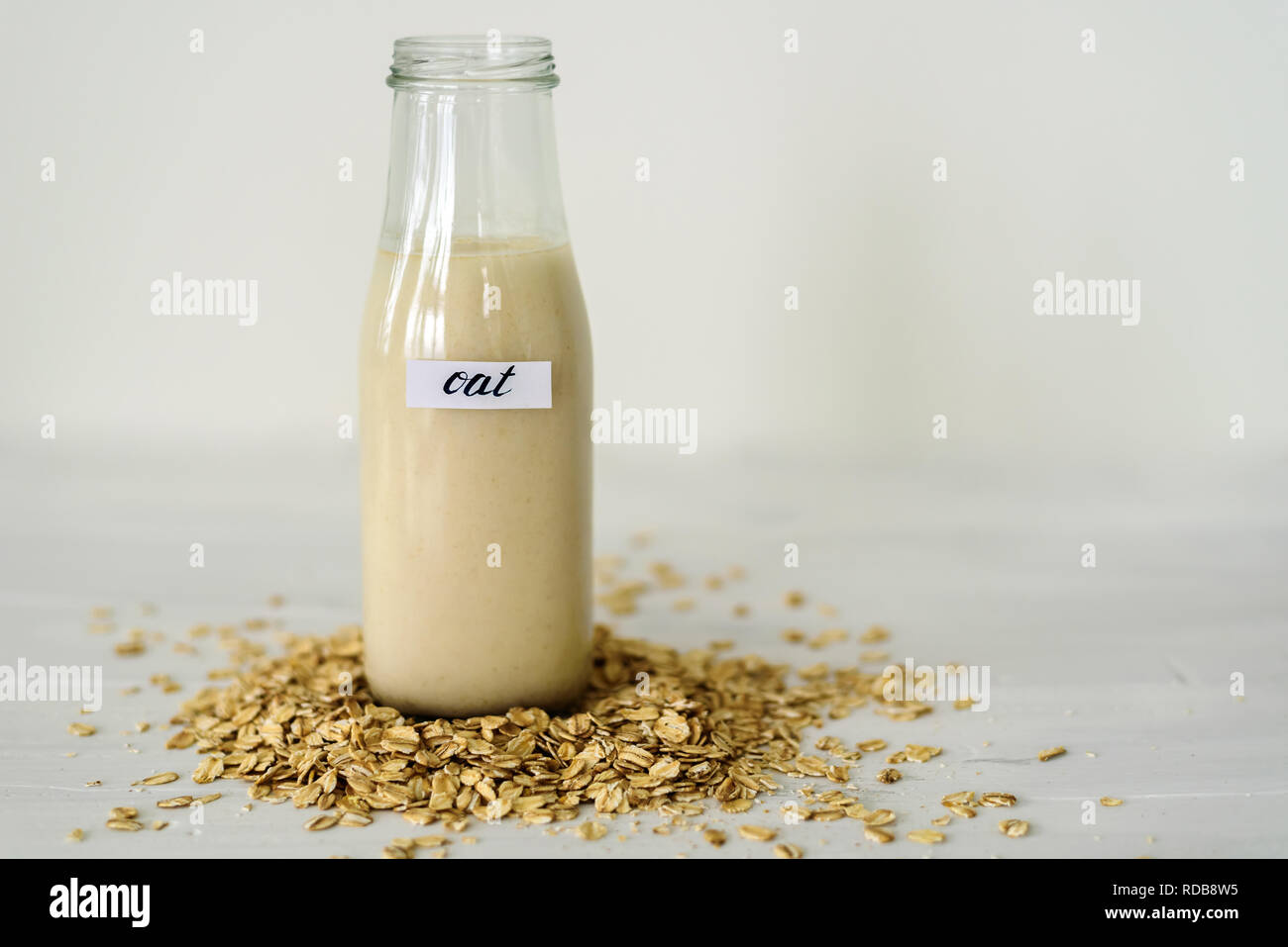 Bouteille verre de lait d'avoine sur fond blanc derrière tas de flocons d'avoine Banque D'Images