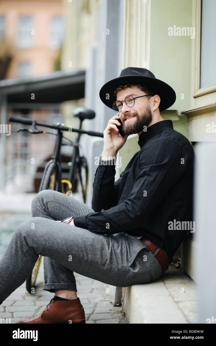 Bel homme barbu en costume classique est à l'aide d'un téléphone intelligent et souriant tout en vélo en ville Banque D'Images