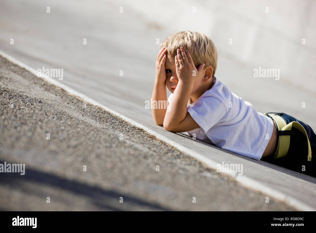 Petit garçon couché sur un trottoir à jouer peek-a-boo Photo Stock - Alamy