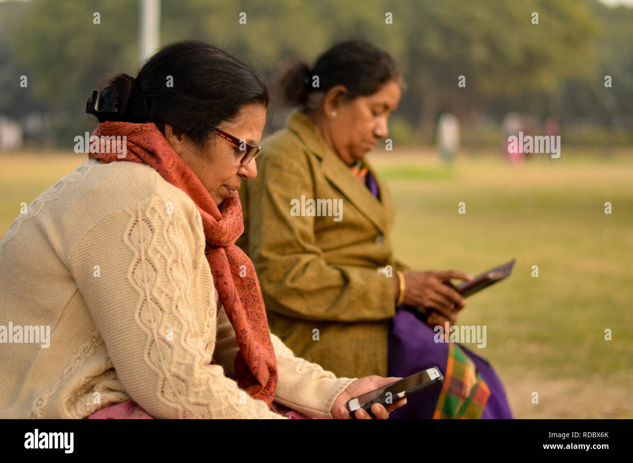 North et South Indian hauts de vieilles femmes utilisant la technologie occupé sur leur smartphone dans un parc extérieur à Delhi hivers. Banque D'Images