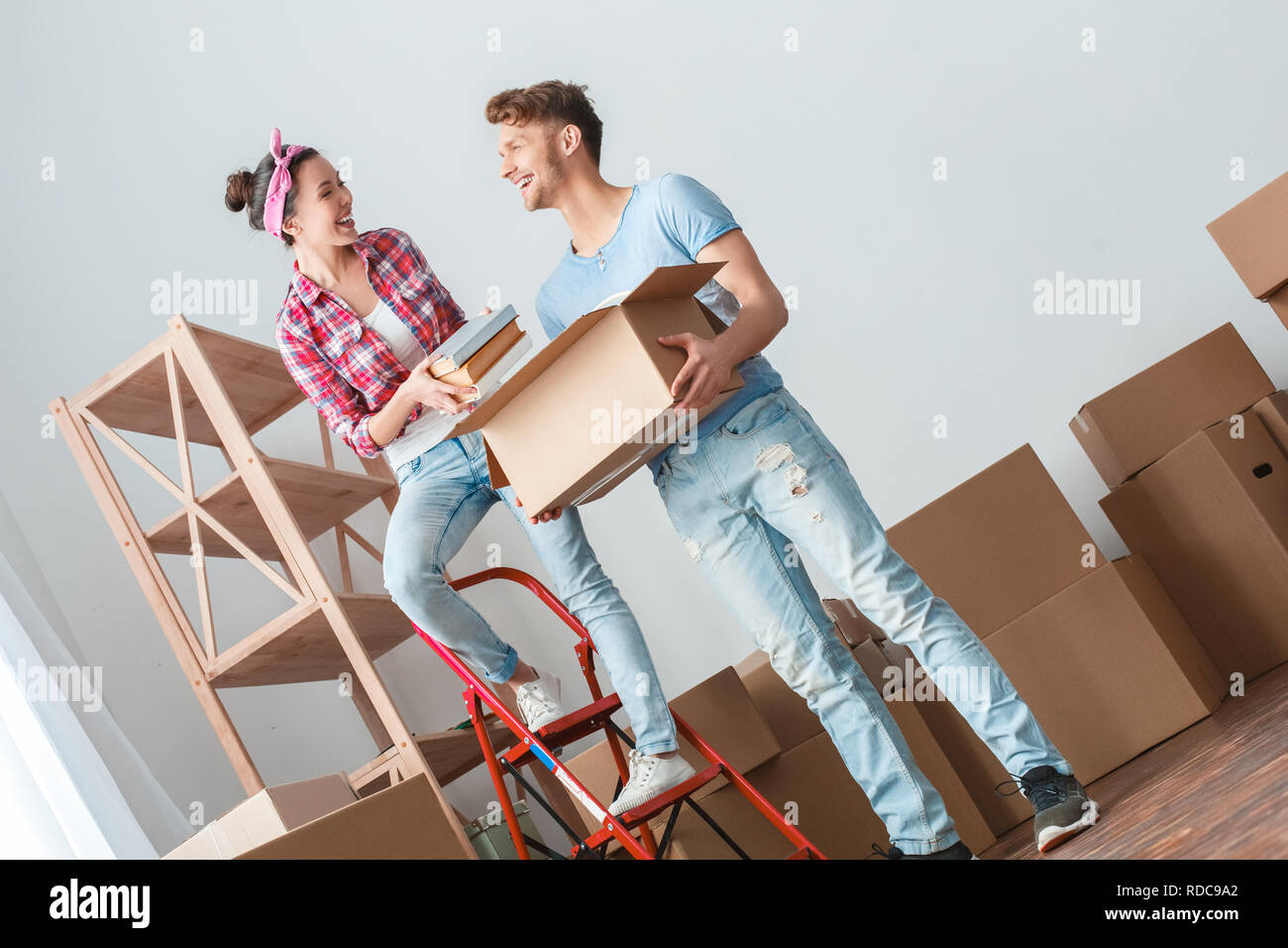 Jeune couple déménagement au nouveau lieu woman standing mettre des livres dans boite à rire enjoué avec l'homme Banque D'Images