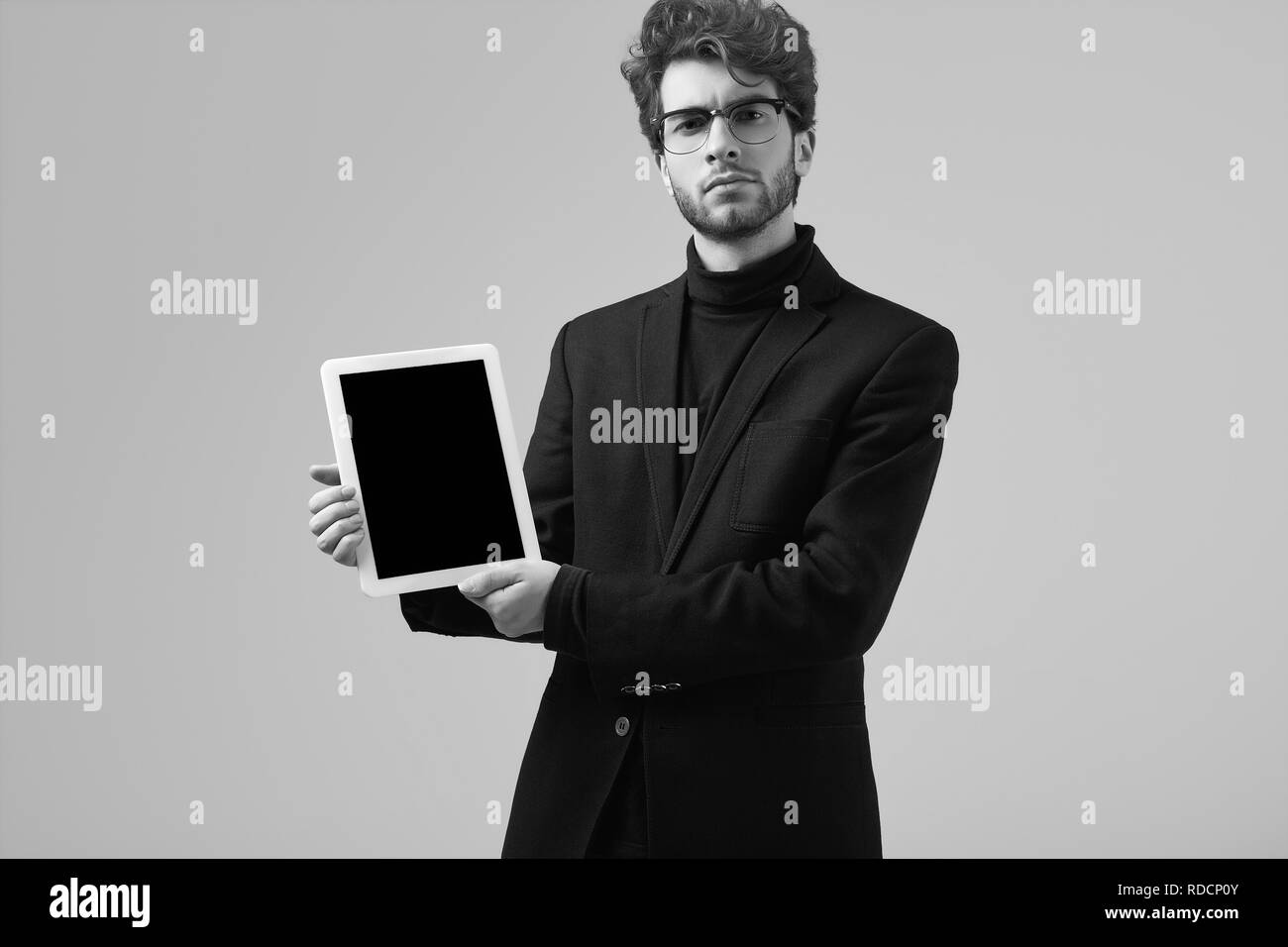 Fashion portrait homme élégant avec de beaux cheveux bouclés portant des lunettes et costume holding a tablet sur fond gris en studio Banque D'Images