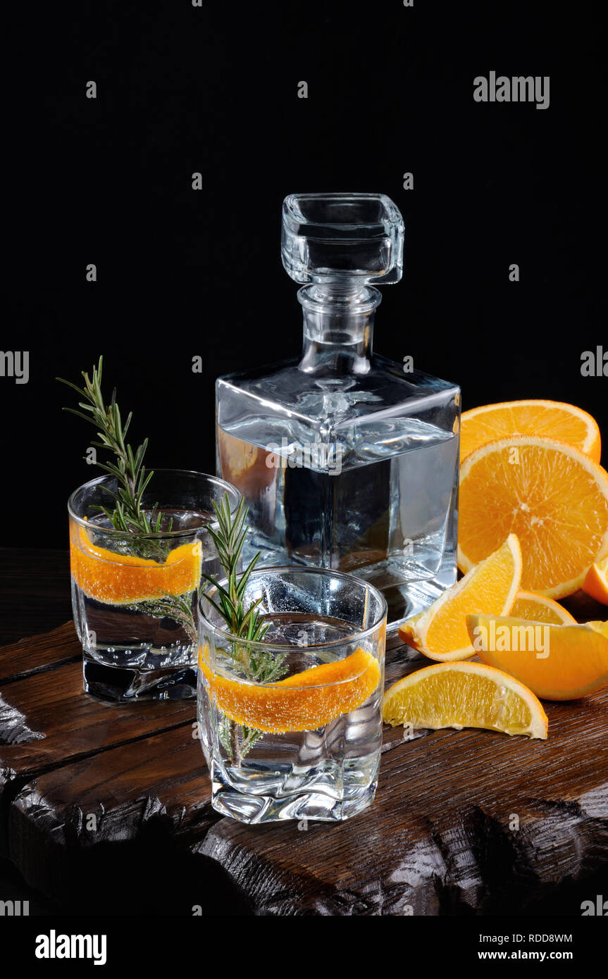 Classique Cocktail Dry Gin Tonic avec et le zeste d'orange avec une branche de romarin sur une planche en bois avec des tranches orange juteuse Banque D'Images