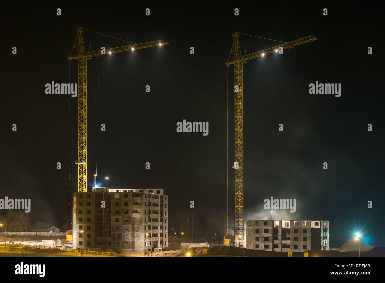 Grues à tour et à plusieurs étages inachevé de hauts bâtiments en construction au chantier éclairé la nuit sur Banque D'Images
