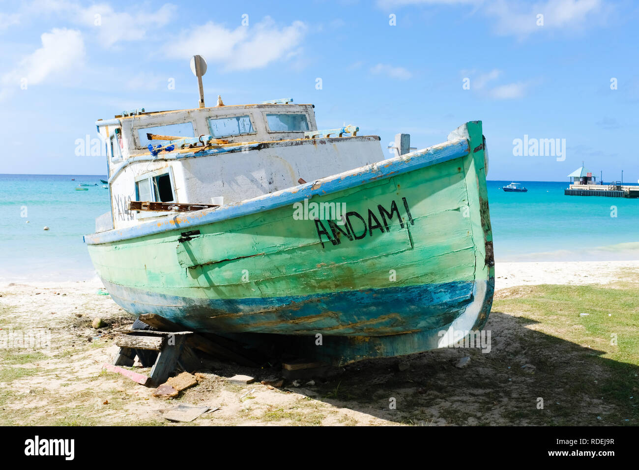 Un bateau de pêche en bois en vert et bleu de la peinture, c'est connu des jours meilleurs, est sur une plage dans les Caraïbes en attente de réparations qui peuvent ne jamais venir Banque D'Images