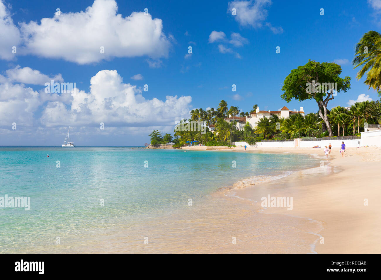 Un yacht anchors off Gibbes Bay, une plage vide avec palmiers et d'un complexe exclusif à son point. Quelques personnes serpentent le long de la plage. Banque D'Images