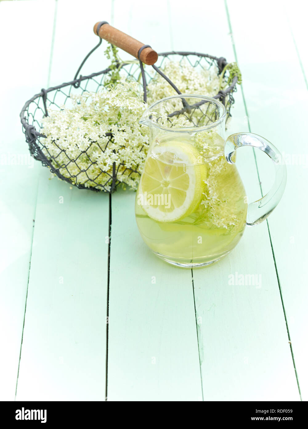 L'infusion aux herbes fraîches des elderflowers et citron dans un pot en verre à côté d'un panier de fleurs fraîchement cueillies sur le bois vert with copy space Banque D'Images