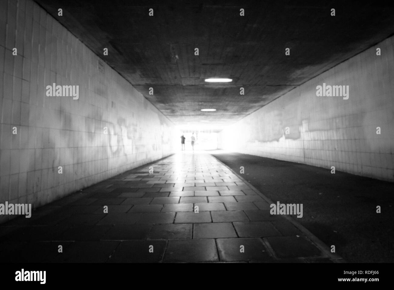La lumière vive à la fin d'un tunnel pour piétons avec silhouette de personnes Banque D'Images