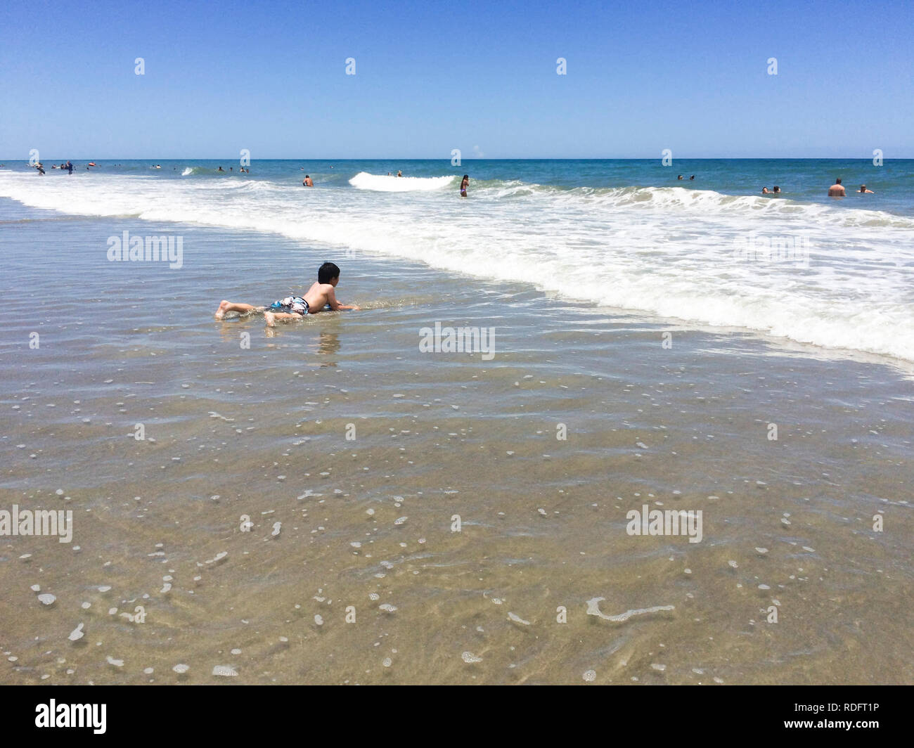 Garçon jouant sur la plage, seul (l'enfant couché dans l'eau, seul) - Cocoa Beach, Floride USA Banque D'Images