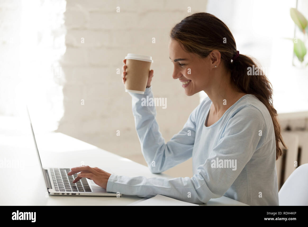 Smiling happy woman using laptop and drinking coffee Banque D'Images