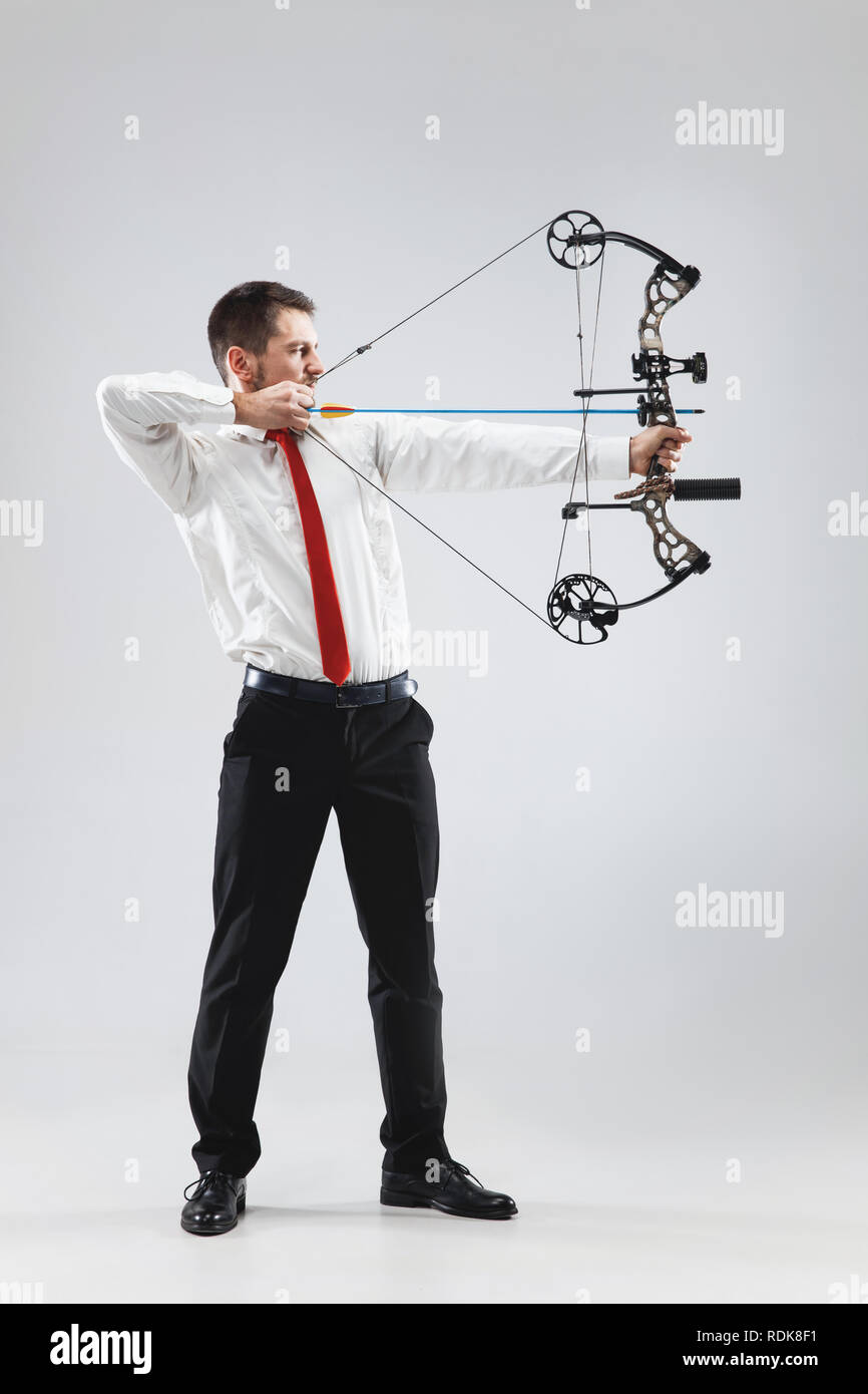 Businessman visant à cibler avec arc et flèche, isolé sur fond studio gris. L'entreprise, objectif, défi, la compétition, l'atteinte concept Banque D'Images