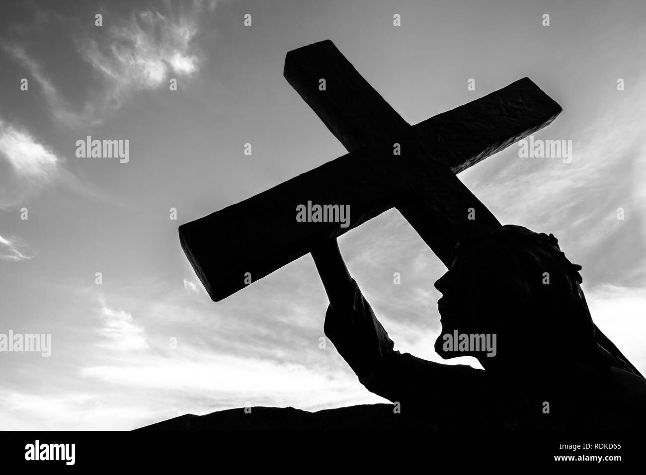 Statue en bronze de Jésus portant sa croix, sur le chemin de sa crucifixion. Idéal pour le concept de Pâques, de la résurrection et de l'autre. Ciel avec nuages sur bac Banque D'Images