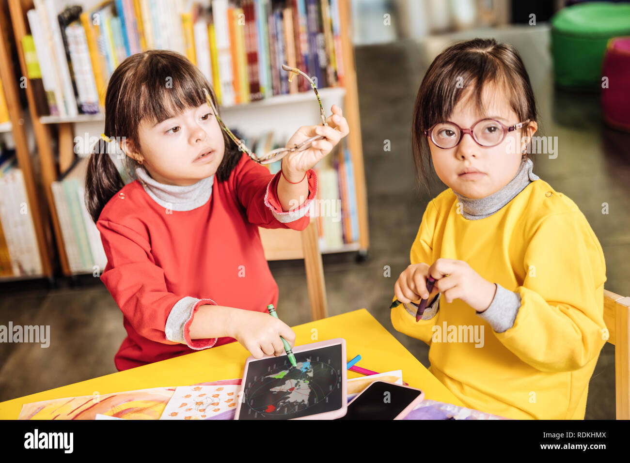 Fille avec le syndrome de assis près de sa sœur en tenant lunettes Banque D'Images