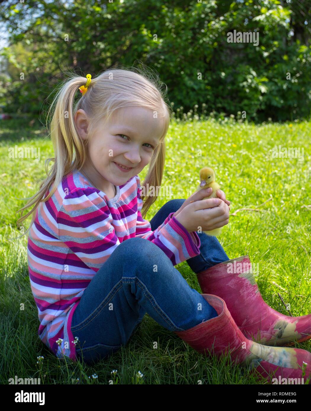 Fille blonde avec petit canard assis sur l'herbe en plein air Banque D'Images