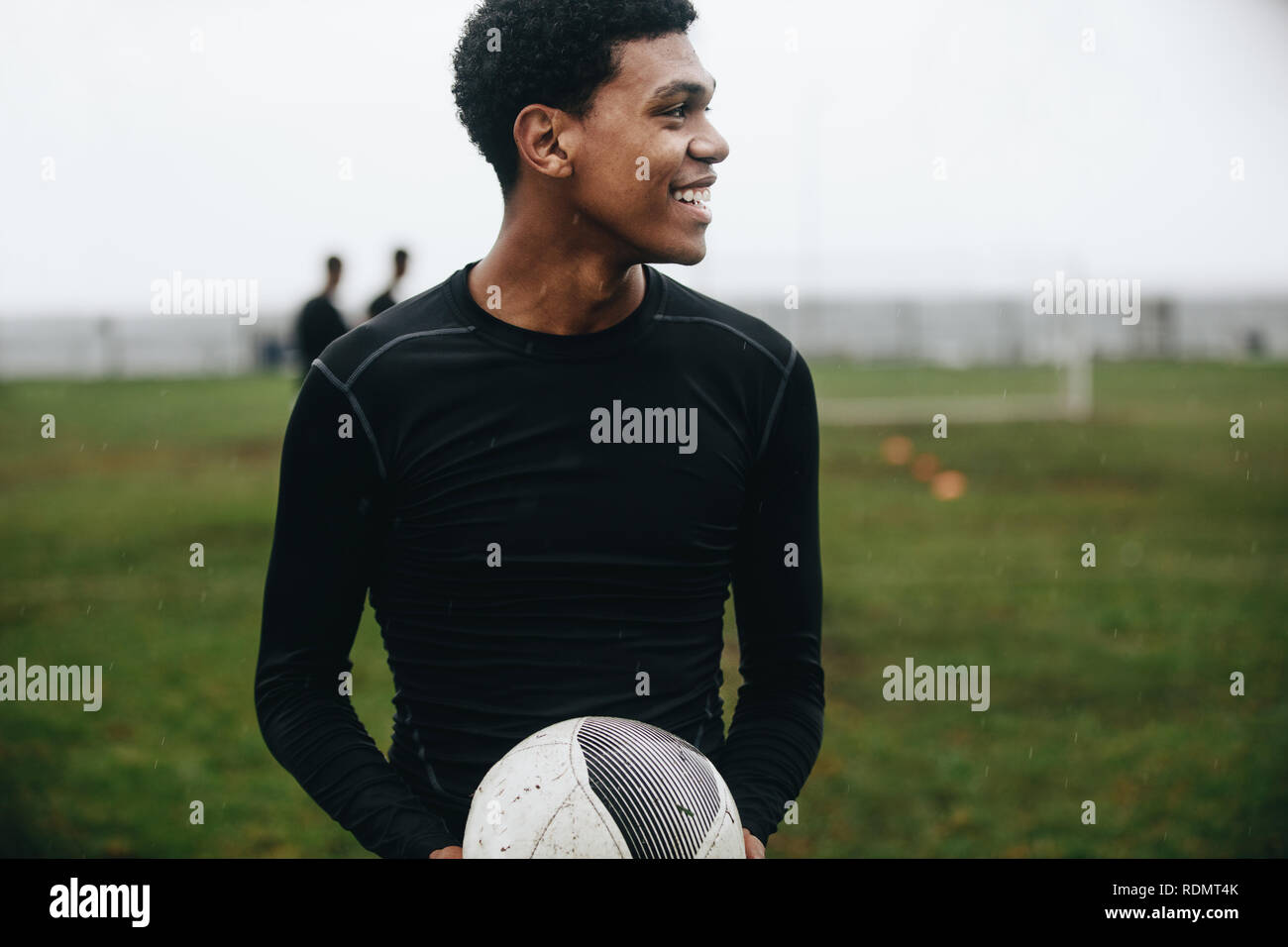 Smiling soccer player standing on field holding a football à la route. Cheerful soccer player exerçant dans la matinée sur terrain avec ses coéquipiers jouer Banque D'Images