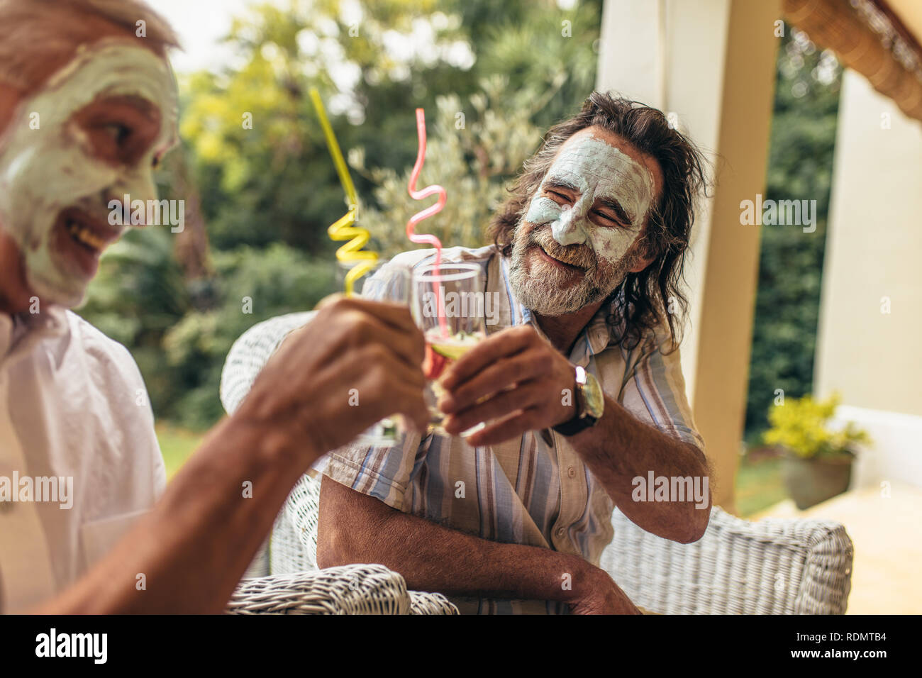Happy old people toasting verres de jus avec masque à l'argile sur le visage. Funny senior Hommes assis ensemble avec masque de visage buvez du jus. Banque D'Images