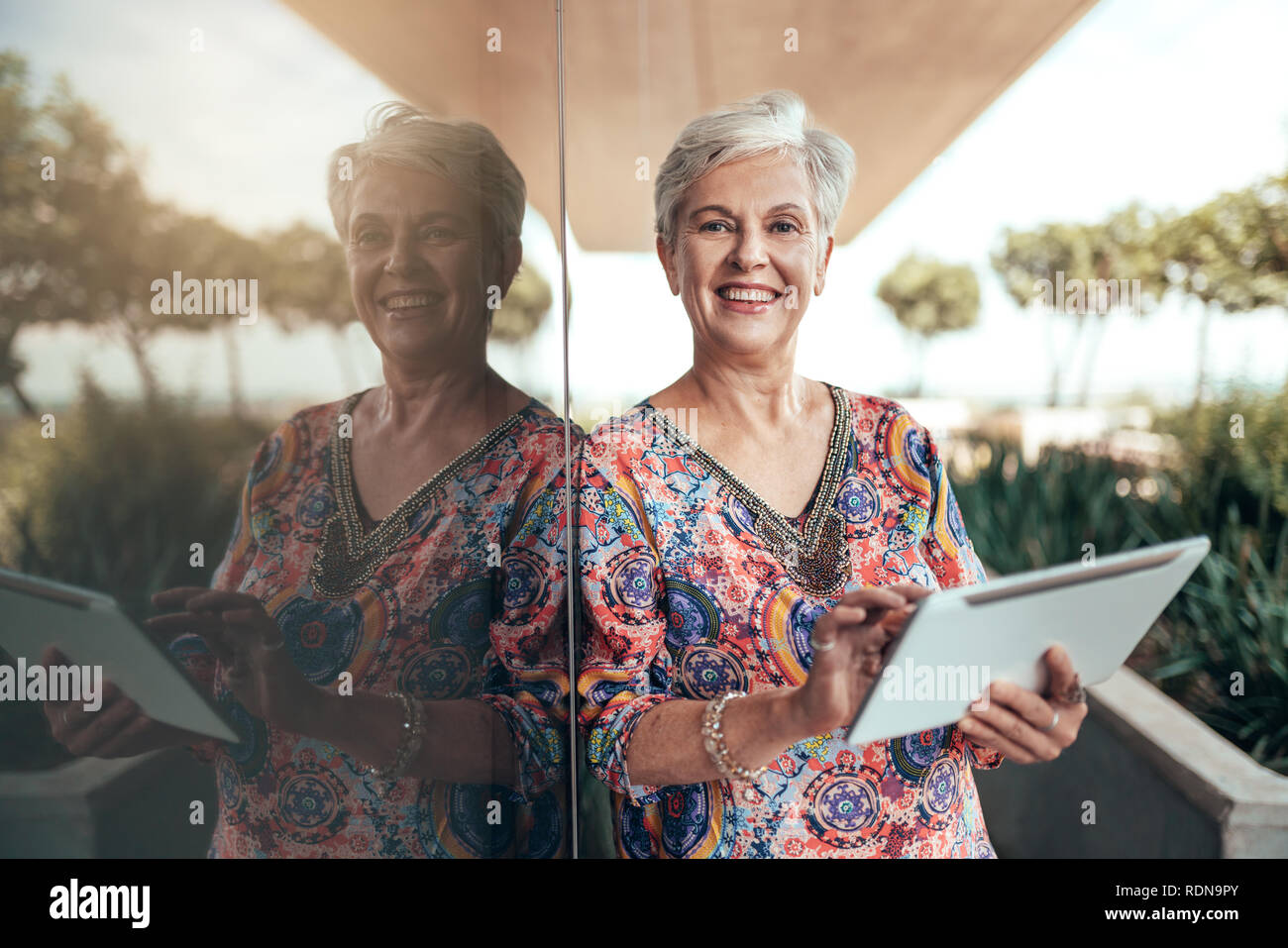 Portrait d'une belle d'âge moyen aux cheveux gris smiling woman working with tablet à la recherche dans l'appareil photo Banque D'Images