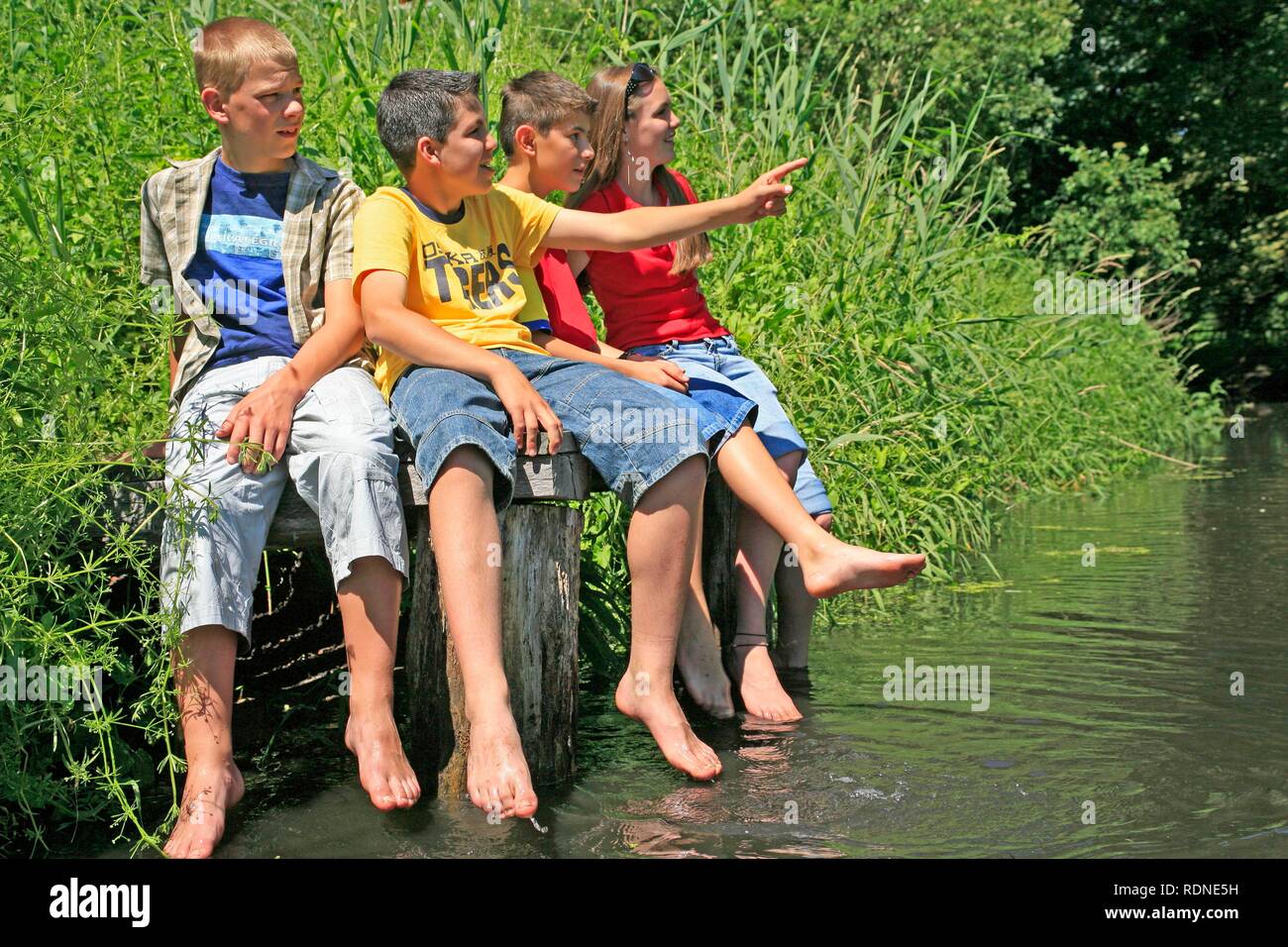 Des enfants assis sur un quai dans un ruisseau et qui traînent leurs jambes dans l'eau, Bad Bodenteich, Basse-Saxe Banque D'Images